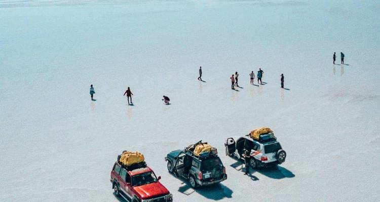 Vehículos todo terreno y figuritas diminutas dispersas por un interminable salar que brilla como espejo bajo un cielo despejado