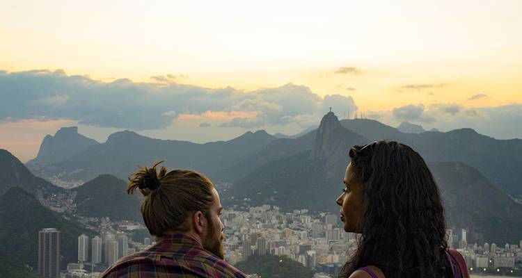 Una pareja contempla el horizonte de Río de Janeiro al atardecer con la estatua del Cristo Redentor posada en un pico distante.