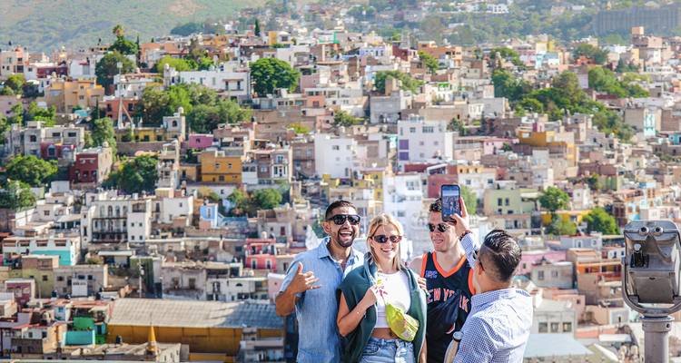 Grupo de amigos se toma una selfie alegre con vista a un vibrante paisaje urbano en la ladera.