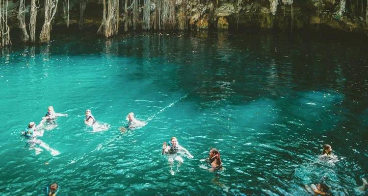 Decenas de nadadores disfrutando del agua turquesa cristalina dentro de una exuberante caverna de cenote.