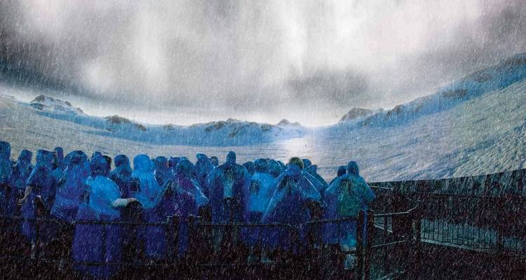 Menigte in blauwe ponchos op een bootdek met uitzicht op de mistige Niagarawatervallen te midden van spattend water en regen
