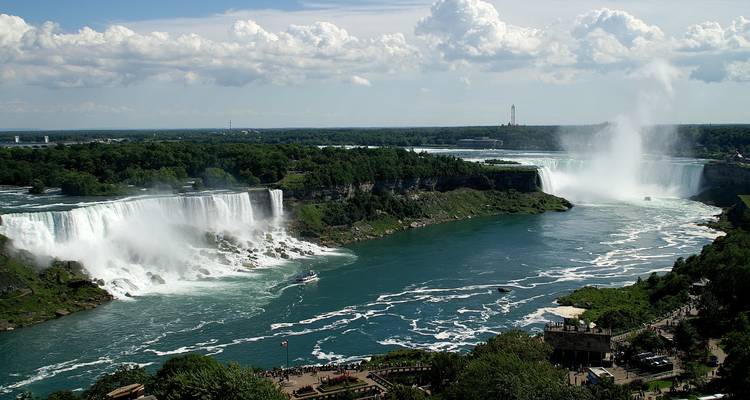 Wijd uitzicht op de Amerikaanse en Hoefijzervallen met kolkend turquoise water en opstijgende mist in een gedeeltelijk bewolkte hemel
