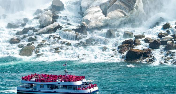 Rondvaartboot vol toeristen in rode ponchos nadert de brullende witte stroomversnellingen aan de voet van de Niagarawatervallen