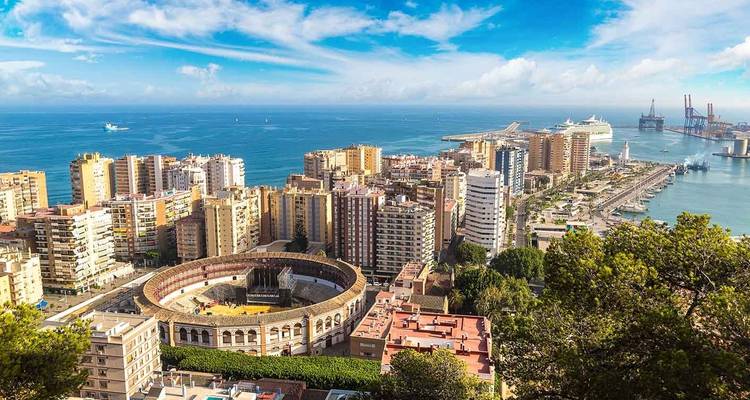 Panorama costero amplio de Málaga que muestra la plaza de toros, el horizonte de rascacielos y el puerto concurrido junto al Mediterráneo azul.