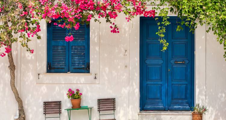 Weiße Gebäudefassade mit blauen Türen und Blumen.