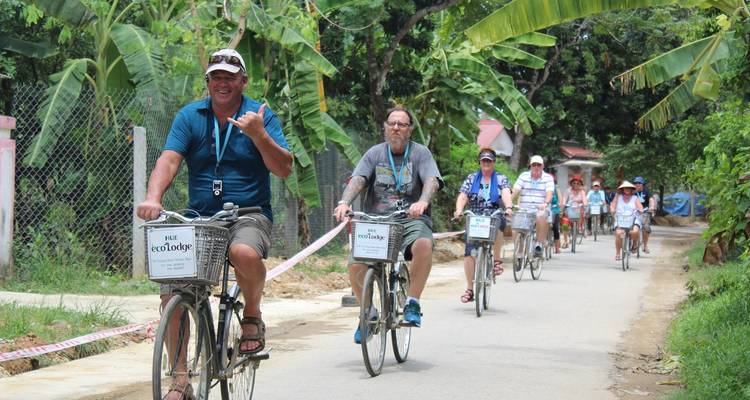 Gruppe von Menschen, die auf einer ländlichen Straße umgeben von Grün Fahrrad fahren.