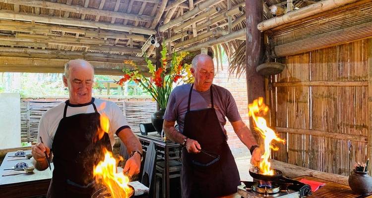 Zwei Männer kochen mit Flammen in einer rustikalen Küchenumgebung.