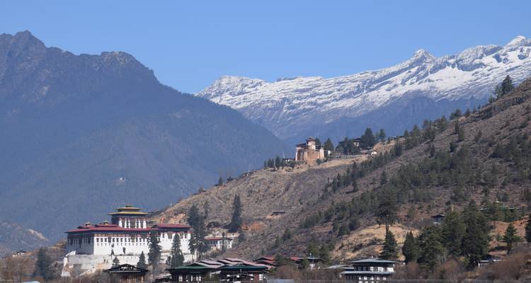 Paisaje montañoso con arquitectura tradicional butanesa y un monasterio en una colina.