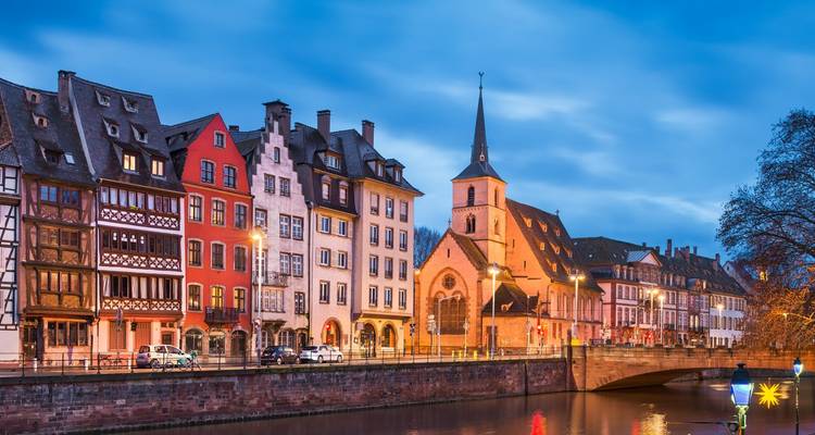 Vista del crepúsculo de coloridos edificios históricos y una pequeña iglesia reflejados en el canal de Estrasburgo.
