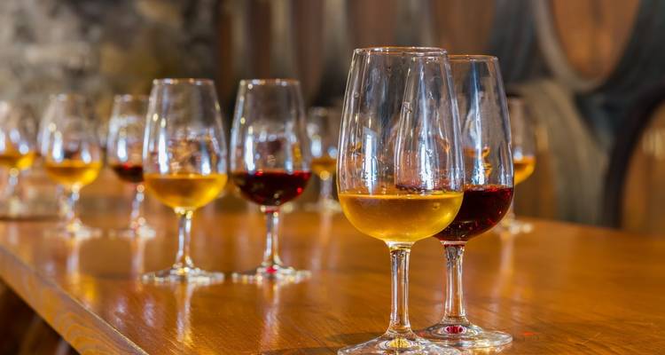 Fila de copas de vino de cristal llenas de oporto dorado y rubí sobre una mesa de cata de madera pulida.