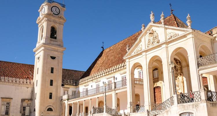 Elegante edificio universitario barroco con alta torre de reloj y fachada con columnatas bajo un cielo azul vívido