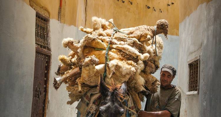 Man die een ezel beladen met goederen door een smalle steeg leidt.