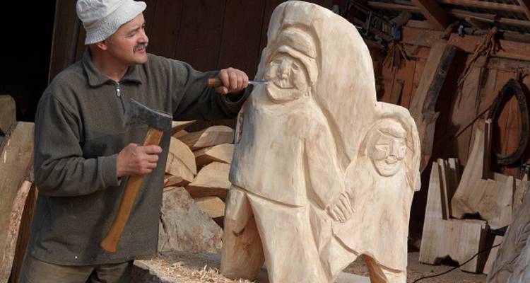 Mann, der in einer Werkstatt eine Holzstatue mit einer Axt schnitzt.