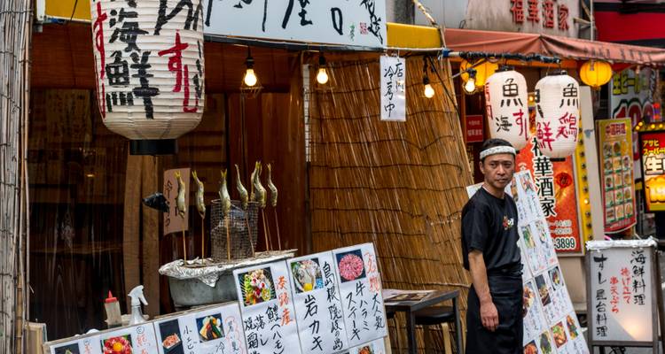 Una tienda local con una persona parada junto a linternas colgantes y menús exhibidos.