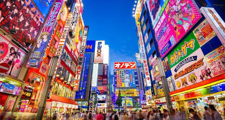 Calle comercial vibrante iluminada por neón con altos edificios cubiertos de letreros y multitudes borrosas de la noche en Tokio.