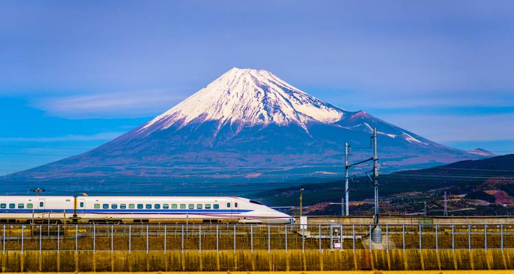 El Monte Fuji nevado se eleva sobre un tren bala Shinkansen que pasa bajo cielos azules despejados.