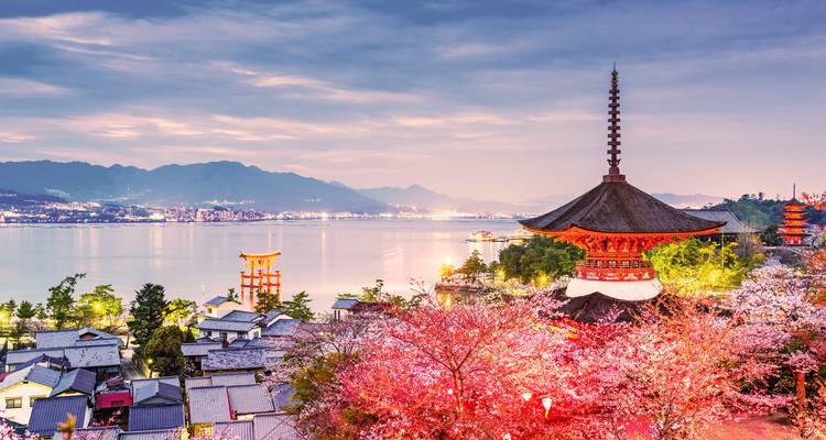 Las flores de cerezo enmarcan pagodas y el famoso torii flotante en la isla de Miyajima al atardecer con vistas a la bahía.