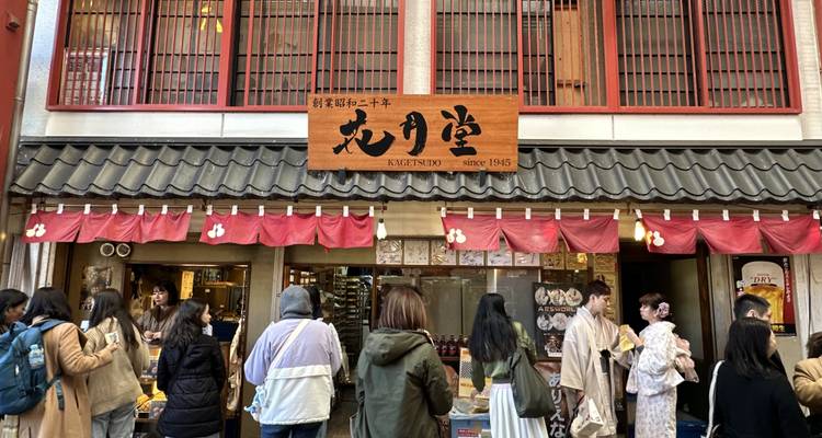 Tienda tradicional de dulces japoneses con clientes y mujeres vestidas con kimono afuera.