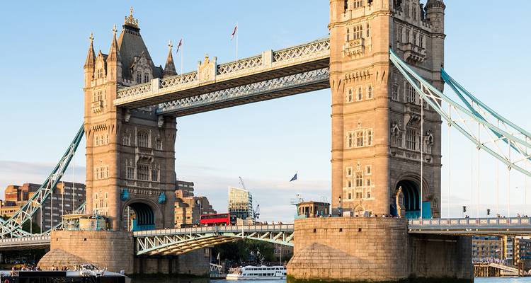 Iconic Tower Bridge spans the Thames River with a classic red double-decker bus crossing in golden light