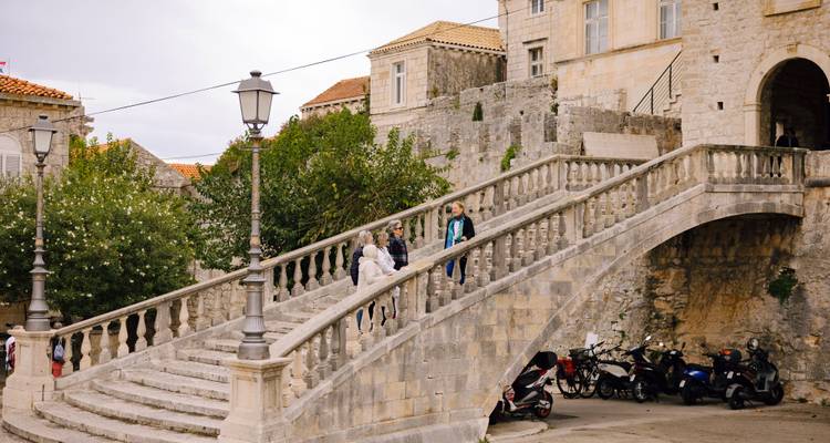 Les voyageurs s'arrêtent sur un élégant escalier en pierre flanqué de lampadaires et de scooters dans une ville historique de l'Adriatique.