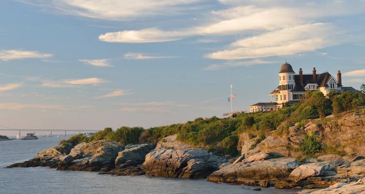 Una mansión costera situada en acantilados rocosos con un puente al fondo.