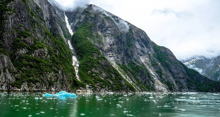 Tall, green mountains rising from a turquoise glacial water body.