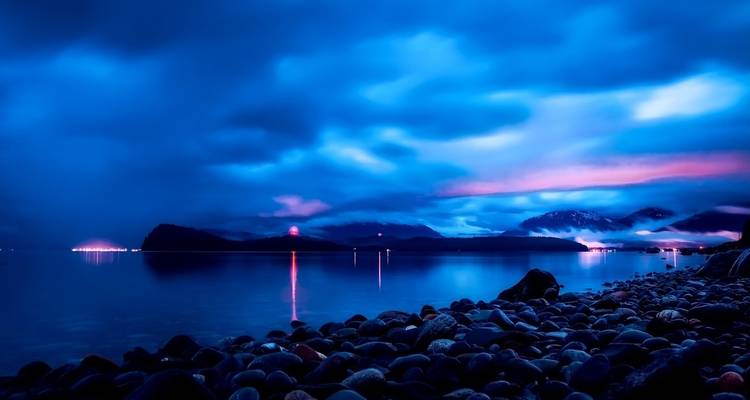 Misty shoreline with mountains in the distance during sunset.