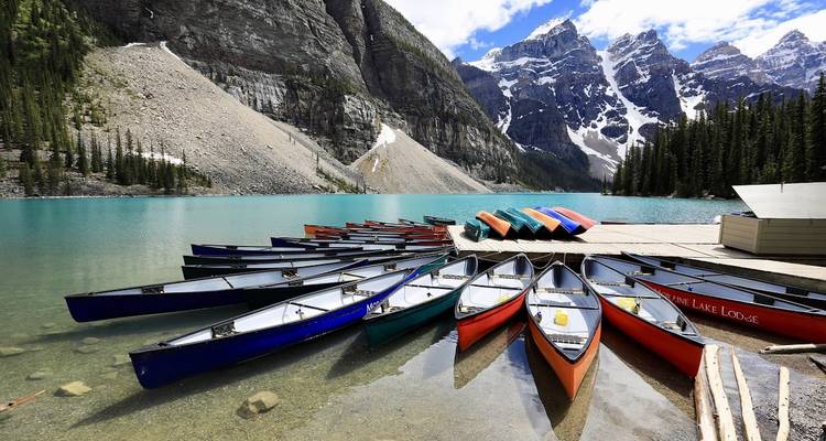 Colorful canoes on a dock with mountains and a lake in the background.