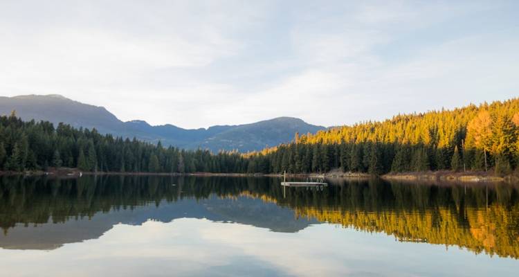 Calm lake with tree reflections surrounded by forested hills.