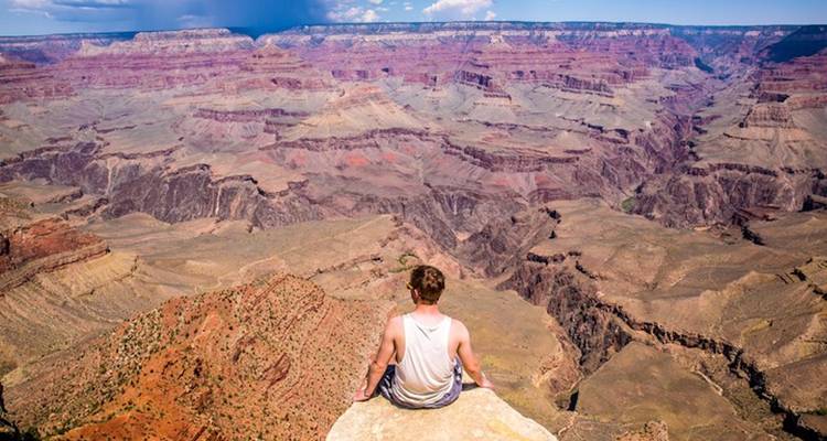 Persoon zittend op de rand van een klif met uitzicht op de Grand Canyon.