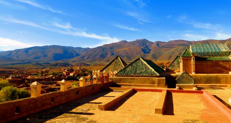 Dächer traditioneller Gebäude mit grünen Ziegeln vor einer bergigen Kulisse.