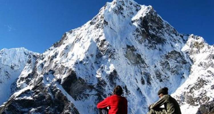 Zwei Menschen sitzen und schauen auf einen schneebedeckten Berggipfel.