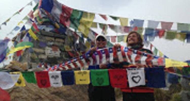 Zwei Personen mit bunten Gebetsfahnen um sie herum.