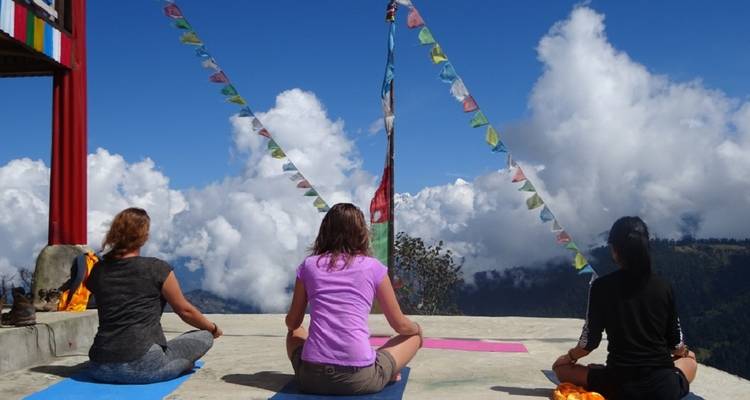 Group of people meditating on a mountain platform with prayer flags.
