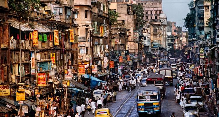 Belebte Straße in Kolkata mit Geschäften und Bussen.