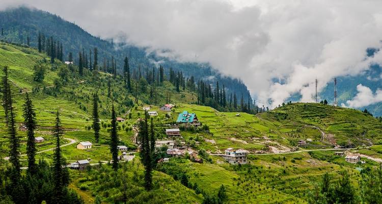Grüne bergige Landschaft mit vereinzelten Häusern und bewölktem Himmel.