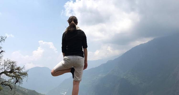 Persoon in een yogahouding met uitzicht op een weelderig berglandschap.