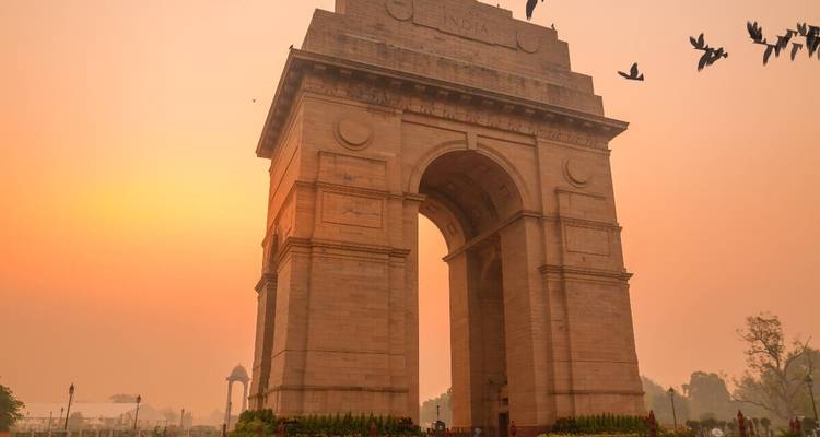 India Gate bij zonsondergang met vogels die door de lucht vliegen.