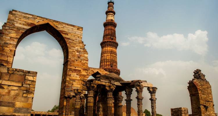 Qutub Minar en ruïnes onder een bewolkte hemel.