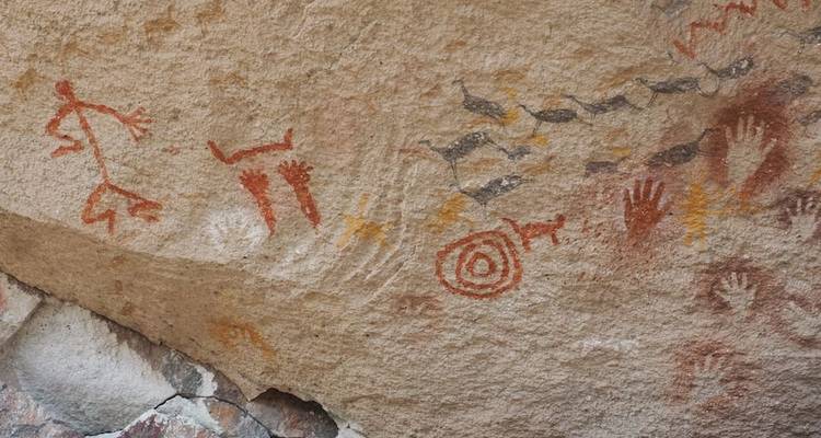 Oude rotstekeningen die handen en dieren afbeelden.
