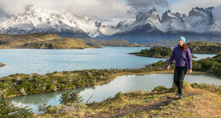 Een wandelaar loopt langs gletsjermeren met de dramatische, met sneeuw bedekte toppen van Torres del Paine die erachter oprijzen.