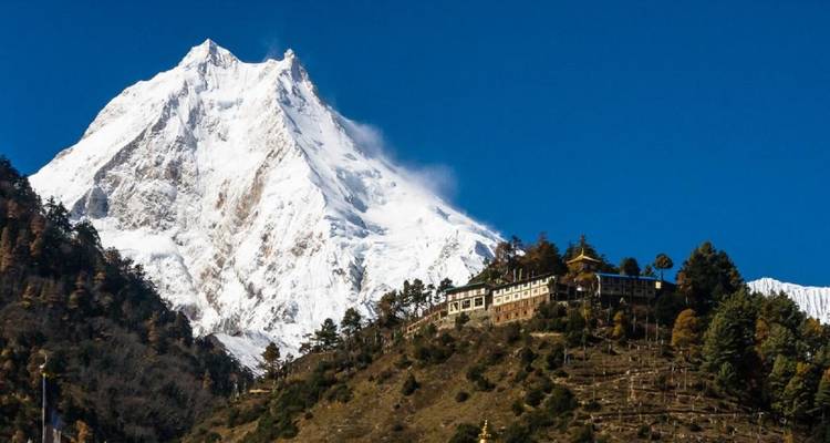 Une chaîne de montagnes enneigée avec un monastère au premier plan.