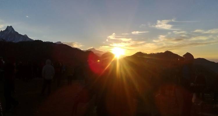 Zonsondergang boven bergen met verzamelde mensen, gedeeltelijk gesilhouetteerd.