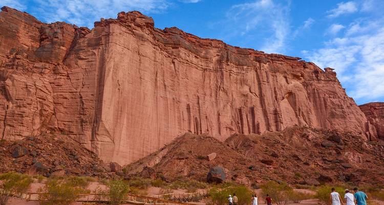 Tall red rock cliffs with people at the bottom.