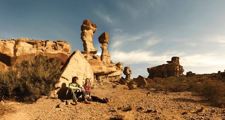 People sitting near large rock formations in a desert landscape.