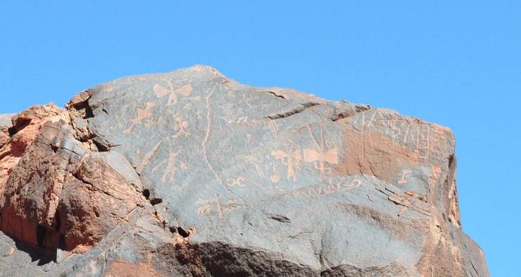 Rock with ancient petroglyphs under a blue sky.
