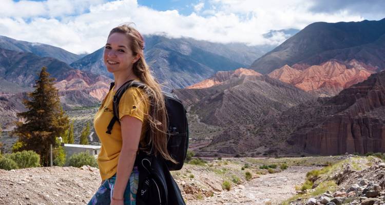 Femme debout sur un sentier devant des montagnes colorées.