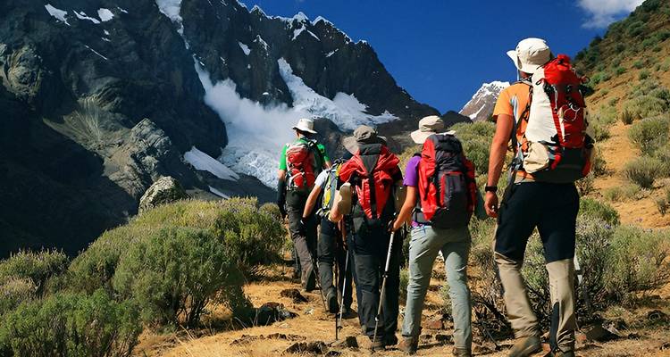Group of hikers ascending a mountain trail with a glacier in the background.