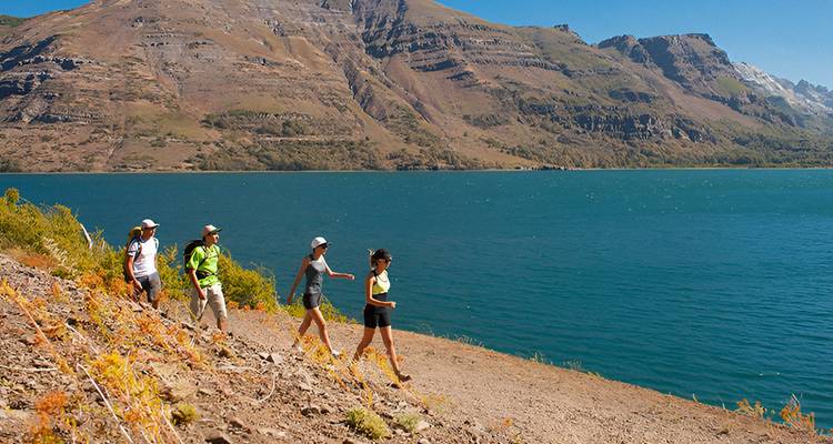 Randonneurs marchant le long d'un lac avec des montagnes en arrière-plan.
