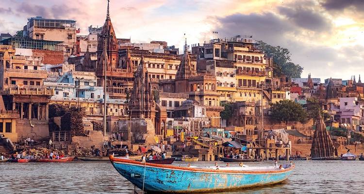 Boten langs een rivieroever met kleurrijke gebouwen en een zonsondergang op de achtergrond.